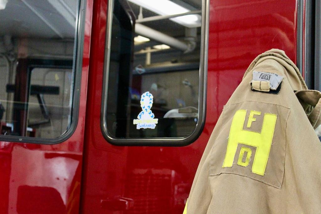 The image shows a fire station with a fire jacket hanging next to a red fire truck, featuring a sticker on the window.
