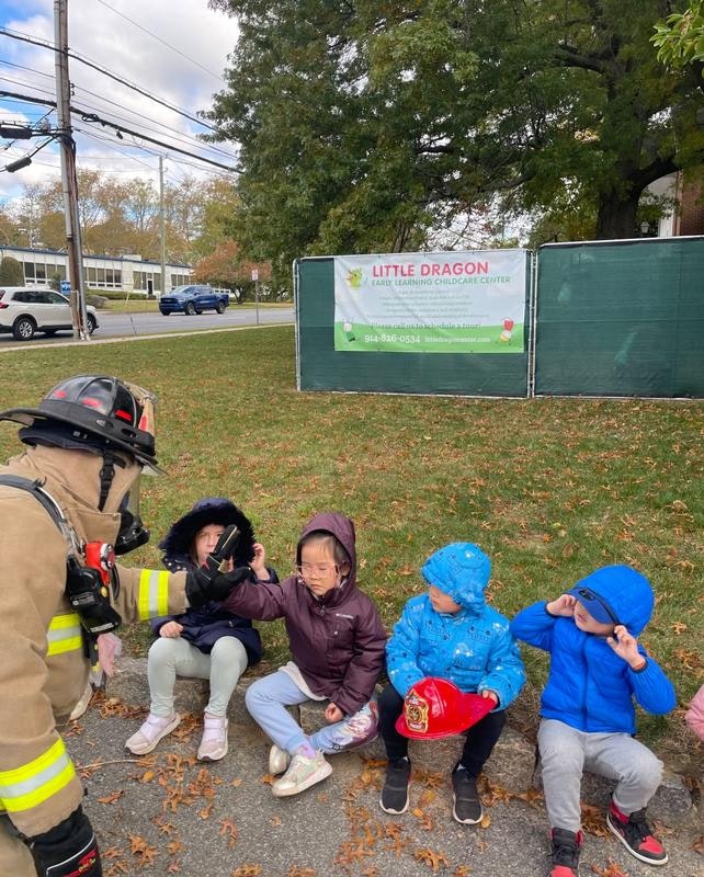 A firefighter interacts with a group of young children outside a childcare center, fostering a fun learning experience.