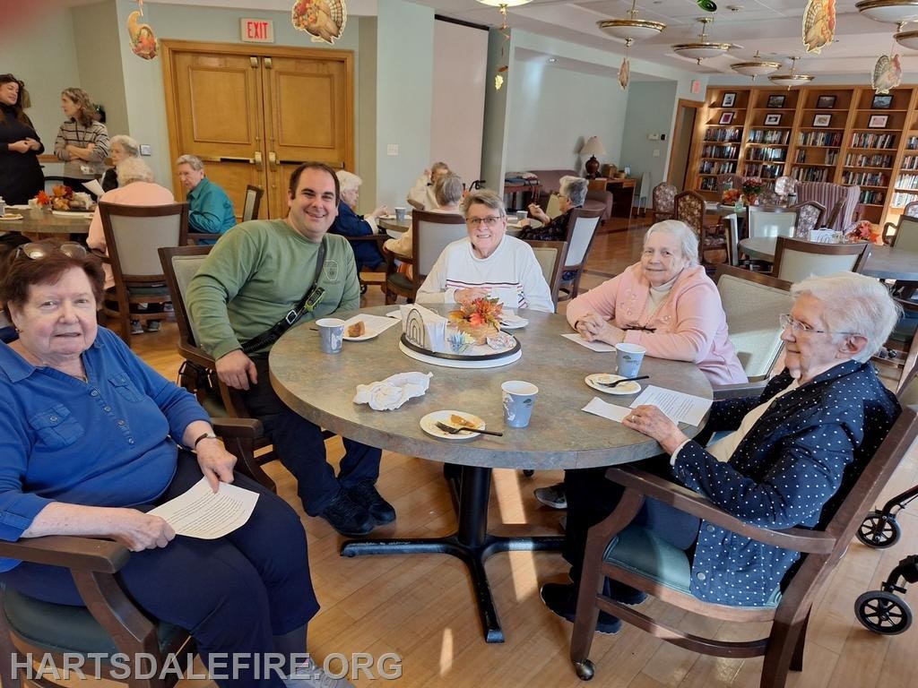 A group of older adults and a man enjoying snacks and drinks around a table in a warm, social setting.