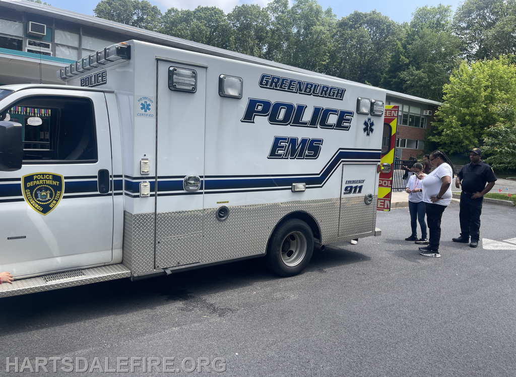 An emergency vehicle marked as Greenburgh Police EMS is parked, with a few people standing nearby.