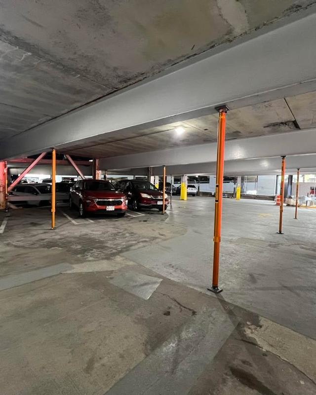 An indoor parking garage with several parked cars and support pillars, featuring a mostly empty space.