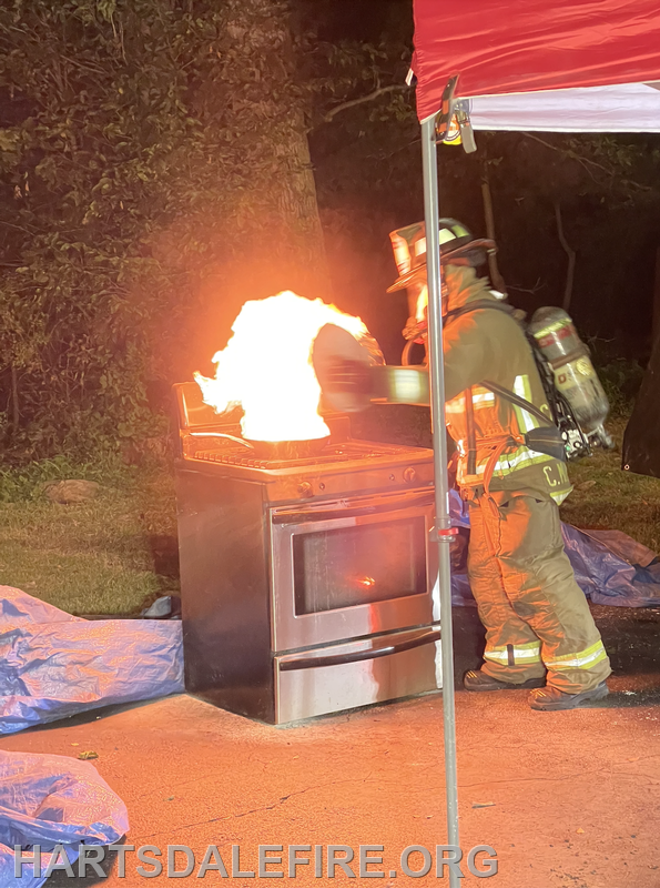 Firefighter extinguishing a flaming stove outdoors during a demonstration.