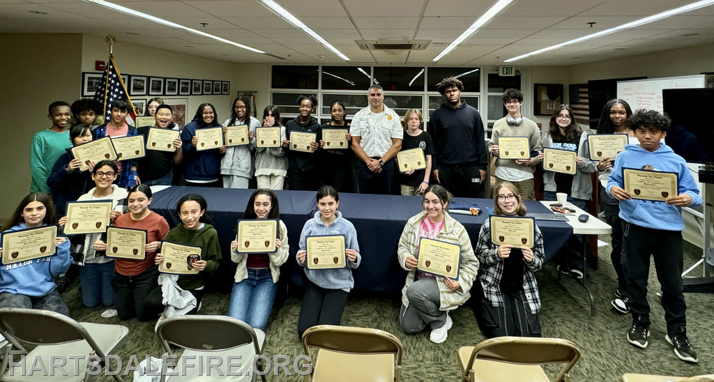 A group of young people holding certificates poses with an instructor, celebrating their achievements in a classroom setting.