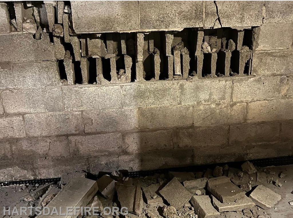 Crumbling brick wall with visible interior damage and debris on the ground.