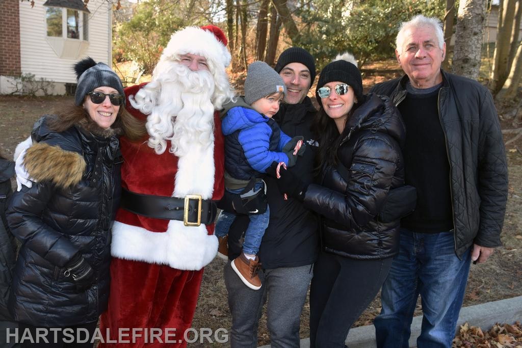 A group of people, including Santa Claus, pose together outdoors in winter attire, smiling and enjoying the festive atmosphere.