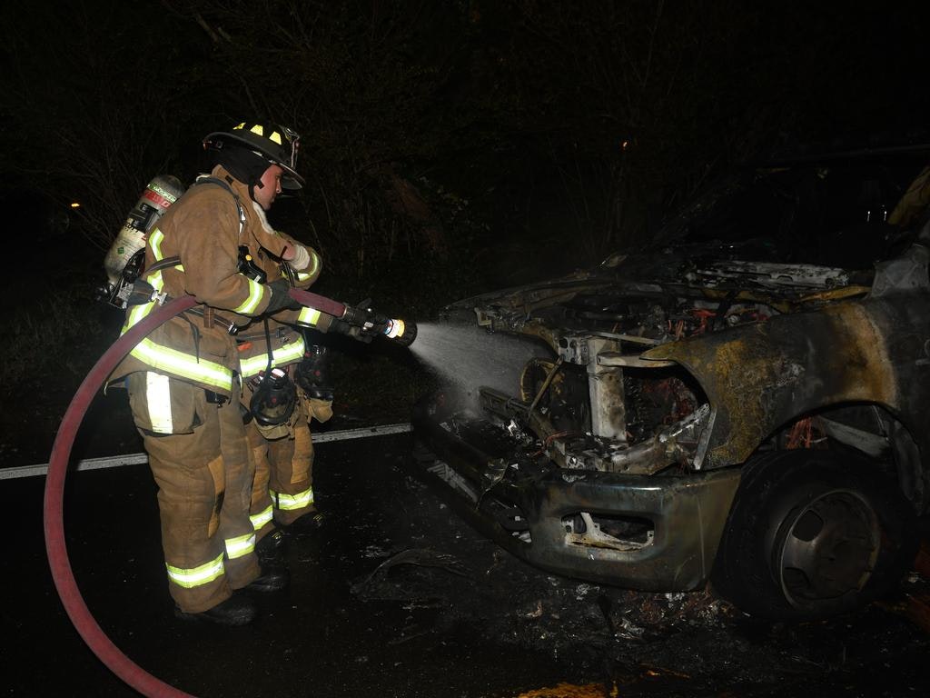 Firefighters extinguish the flames from a burned-out vehicle at night.