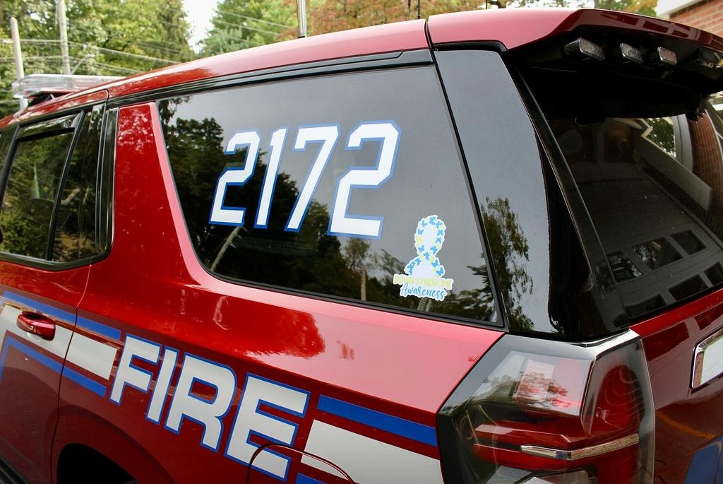 The image shows the rear of a red fire vehicle marked with "FIRE" and the number "2172," along with a blue awareness ribbon sticker.