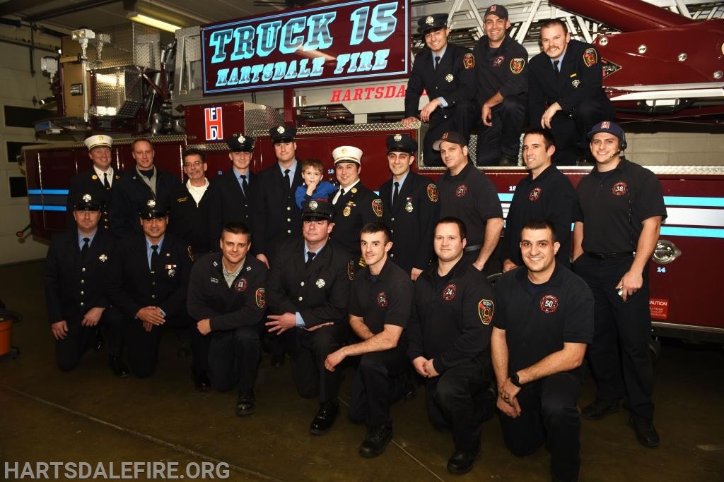 A group of firefighters posing in front of a fire truck labeled "TRUCK 15 HARTSDALE FIRE."