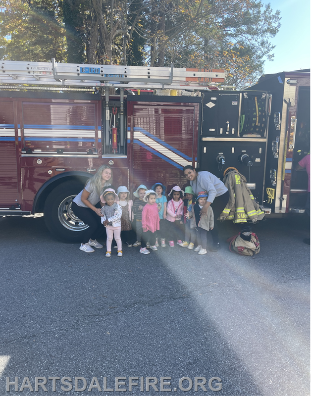 A group of children and two adults pose happily in front of a fire truck.