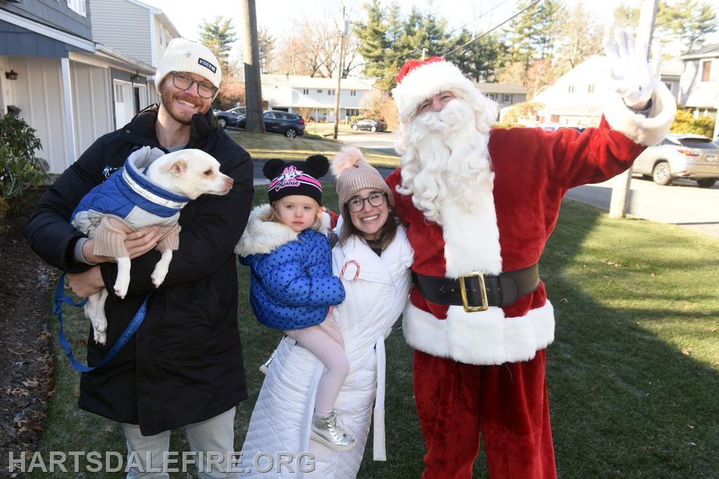 A festive scene with a family, a dog, and Santa Claus, all smiling outdoors in winter attire. Holiday cheer is in the air!