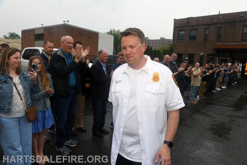 A crowd is applauding as a man in a white shirt walks past, suggesting a significant event or recognition.