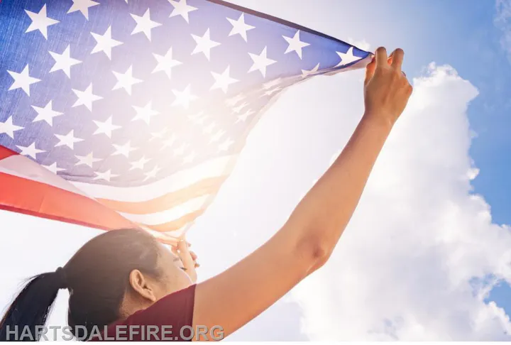 Person holding an American flag against a bright, cloudy sky.