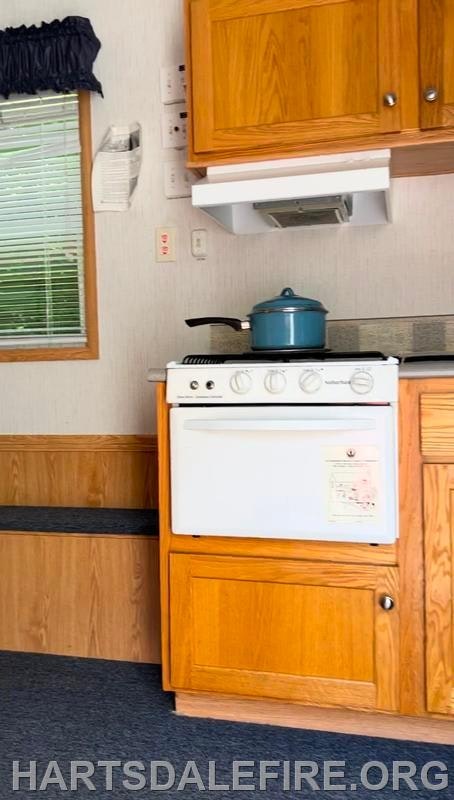 Small kitchen area with wooden cabinets, a stove, and a blue pot on the burner.