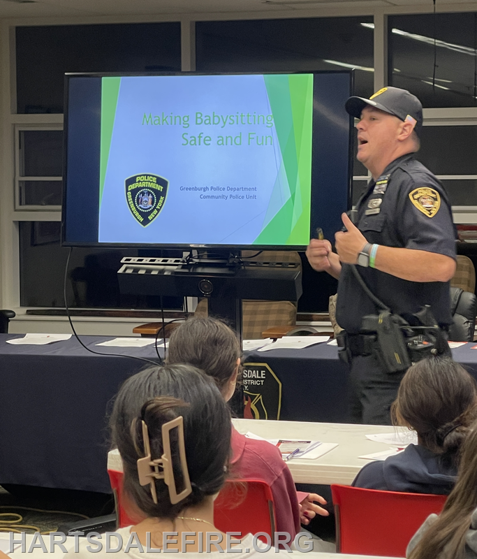 A police officer presents a workshop titled "Making Babysitting Safe and Fun" to an audience, emphasizing safety tips.