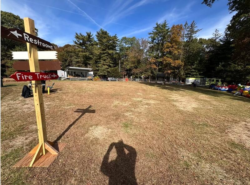 A signpost indicating directions to restrooms and a fire truck, with an open grassy area and trees in the background.