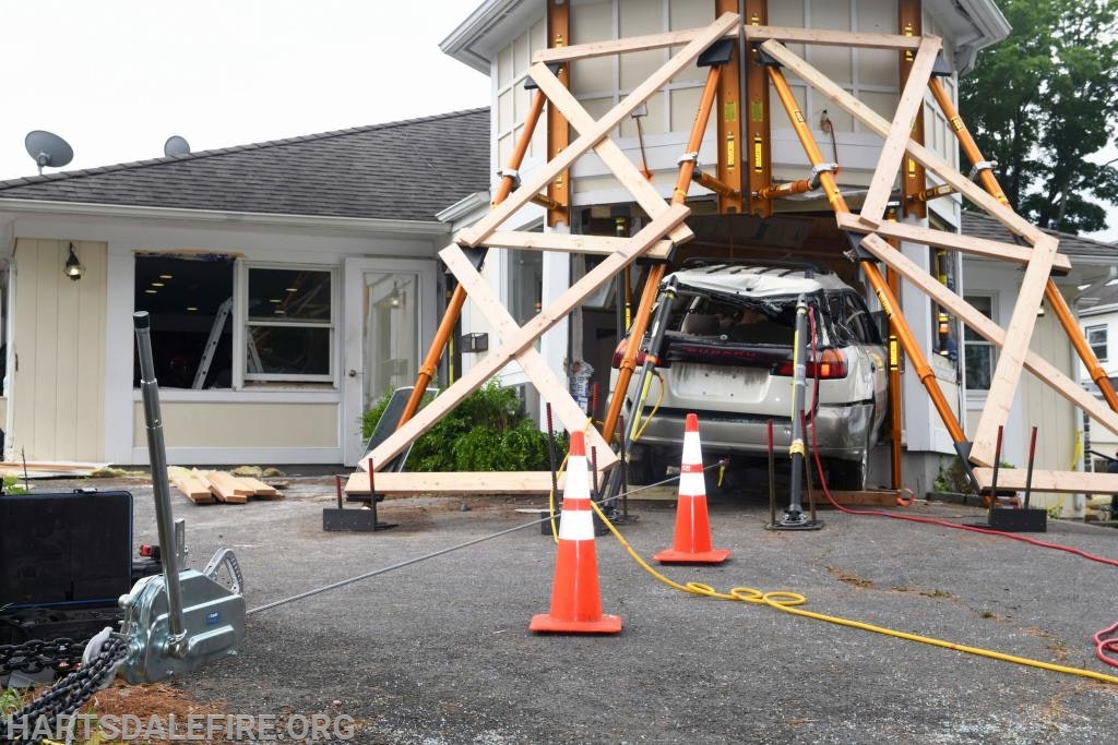 A car crashed into a building, supported by wooden beams and cones around, with visible damage and debris.