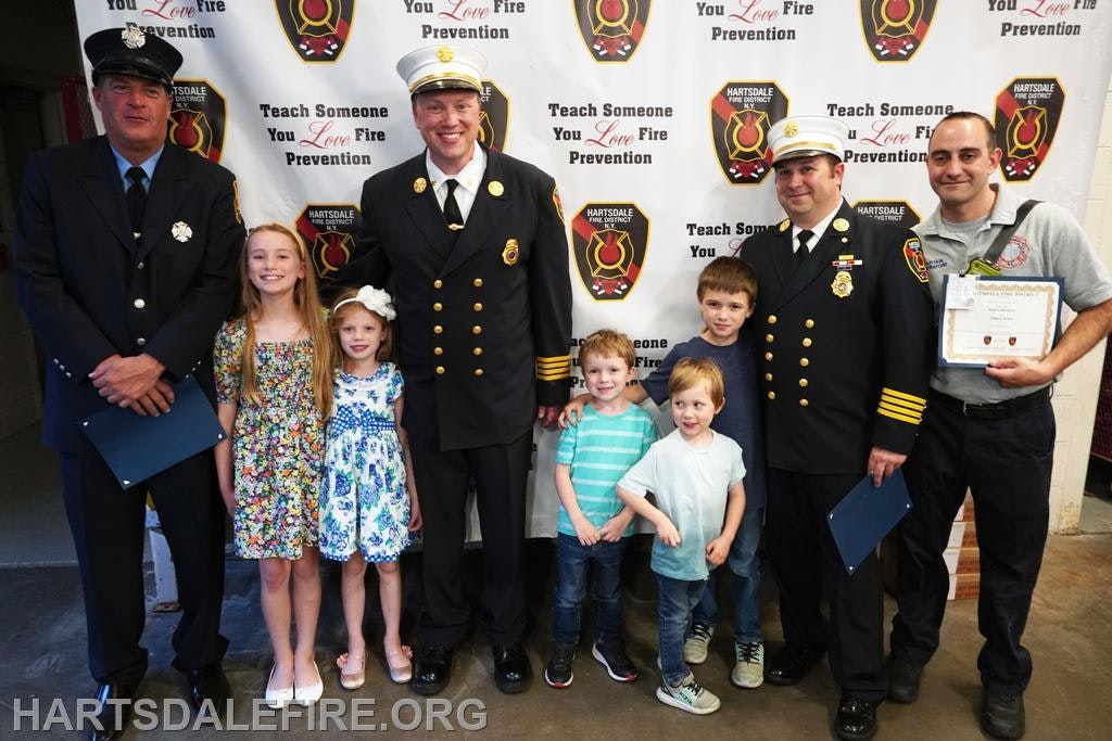Firefighters and children pose for a photo; backdrop promotes fire prevention.
