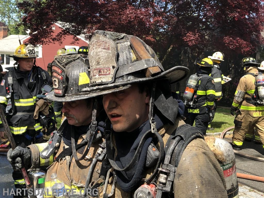 Firefighters in gear at a scene with hoses, helmets, and equipment.