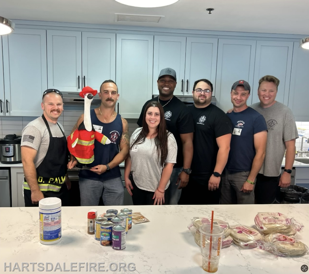 A group of people in a kitchen, with one holding a firefighter-themed puppet and various food items displayed on the counter.