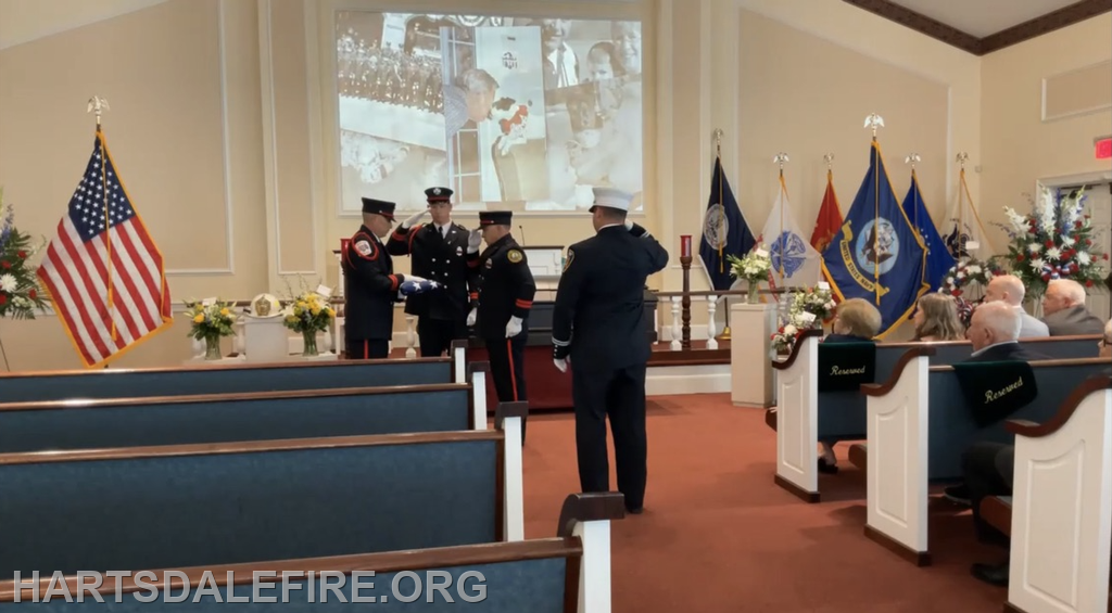 A solemn ceremony with a flag presentation, honoring someone, held in a church decorated with flowers and flags.