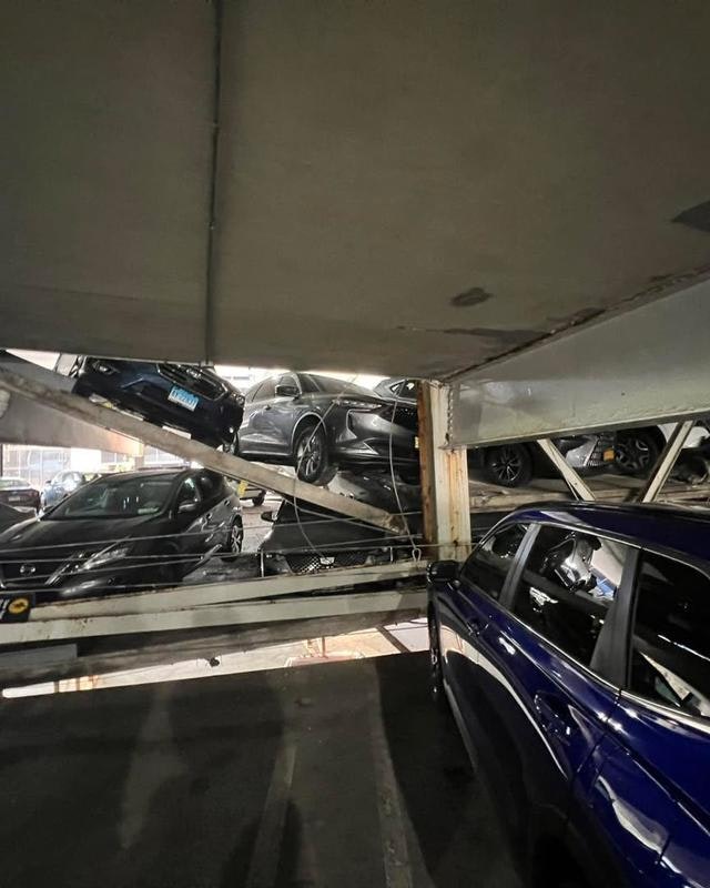 A chaotic scene in a parking garage with cars stacked and partially suspended on a metal frame.