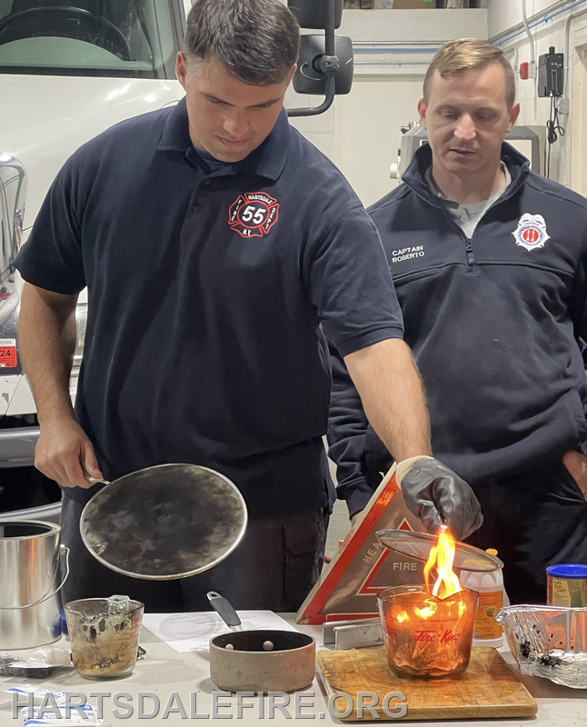 Two firefighters are conducting a fire safety demonstration, with one handling a lit candle and another observing.