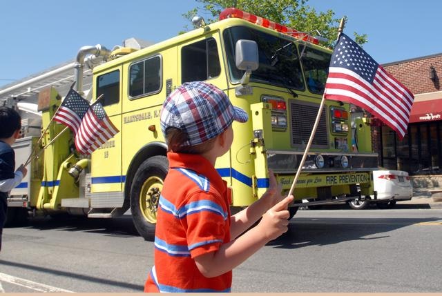 Child waves an American flag near a yellow fire truck during a parade.