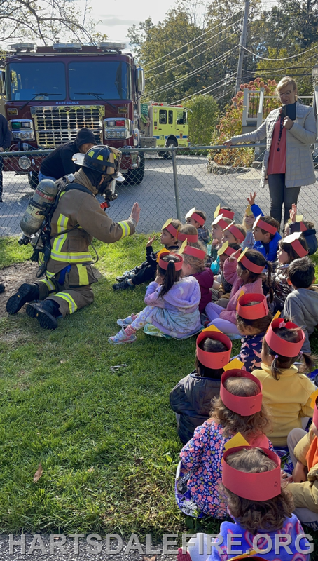 A firefighter interacts with a group of children, who are wearing paper crowns, during a community safety event.