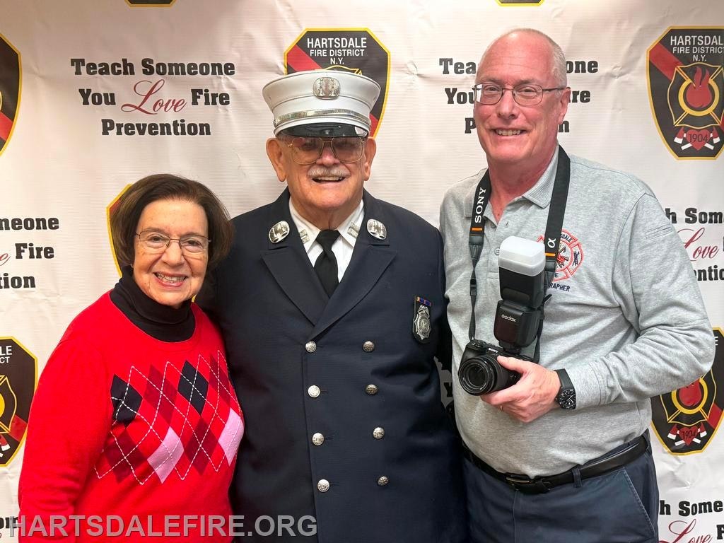 A group photo featuring three people smiling in front of a fire prevention-themed backdrop.