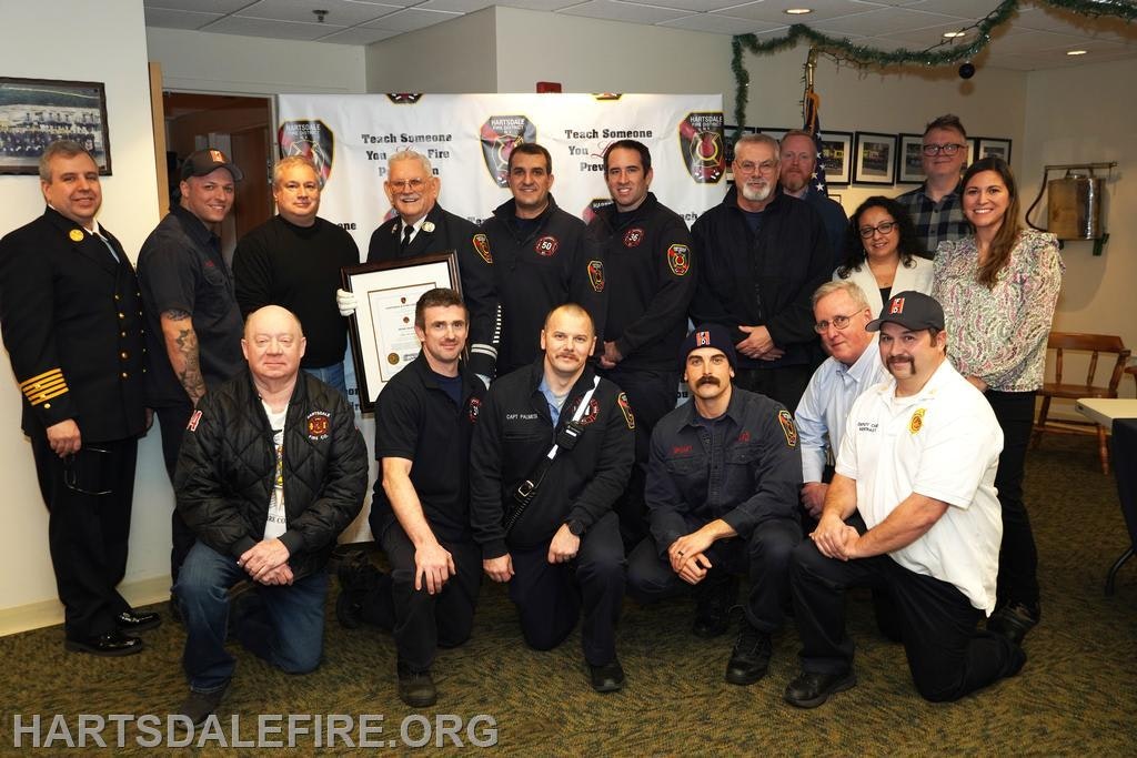 A group photo of firefighters and officials at an event, celebrating the "Teach Someone You Care" fire prevention program.