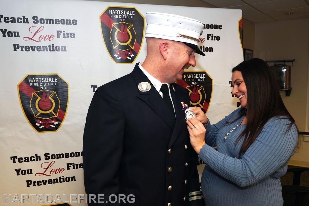 A woman is attaching a badge to a firefighter's uniform at a fire prevention event. Celebratory atmosphere is present.