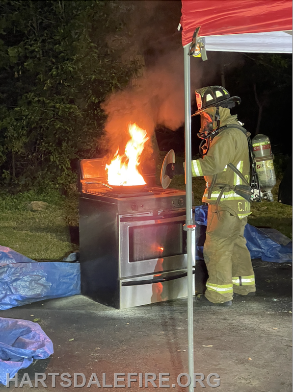 Firefighter in gear manages a stove fire outdoors at night.