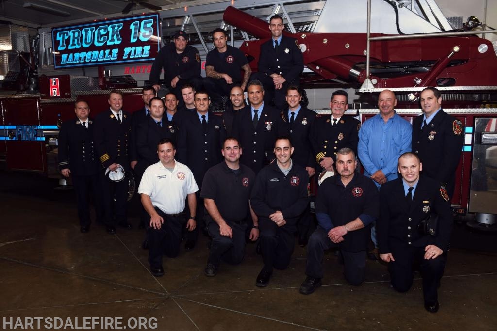 A group of firefighters posed in front of a fire truck labeled "Truck 15 Hartsdale Fire."