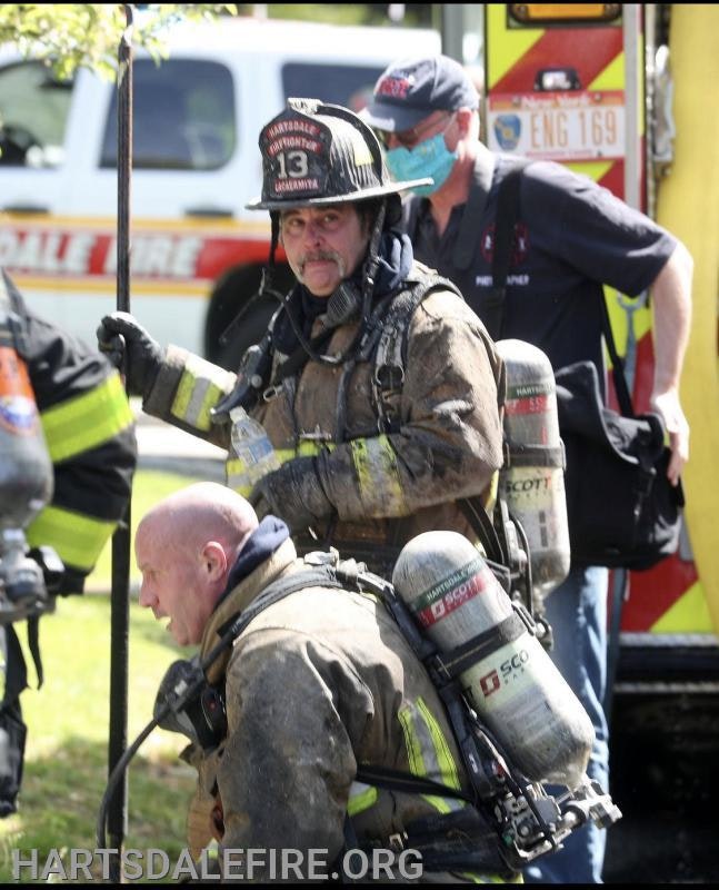 Firefighters in gear and helmets, carrying equipment, in front of a fire truck.