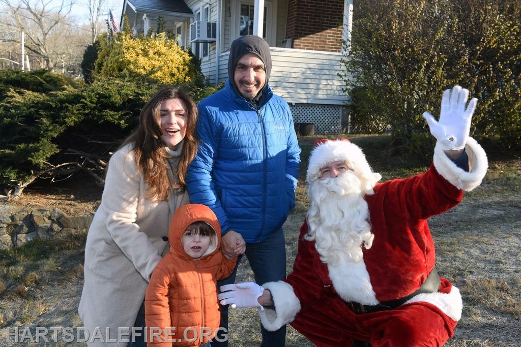 A family poses outdoors with Santa Claus, smiling and enjoying a festive moment in a suburban setting.