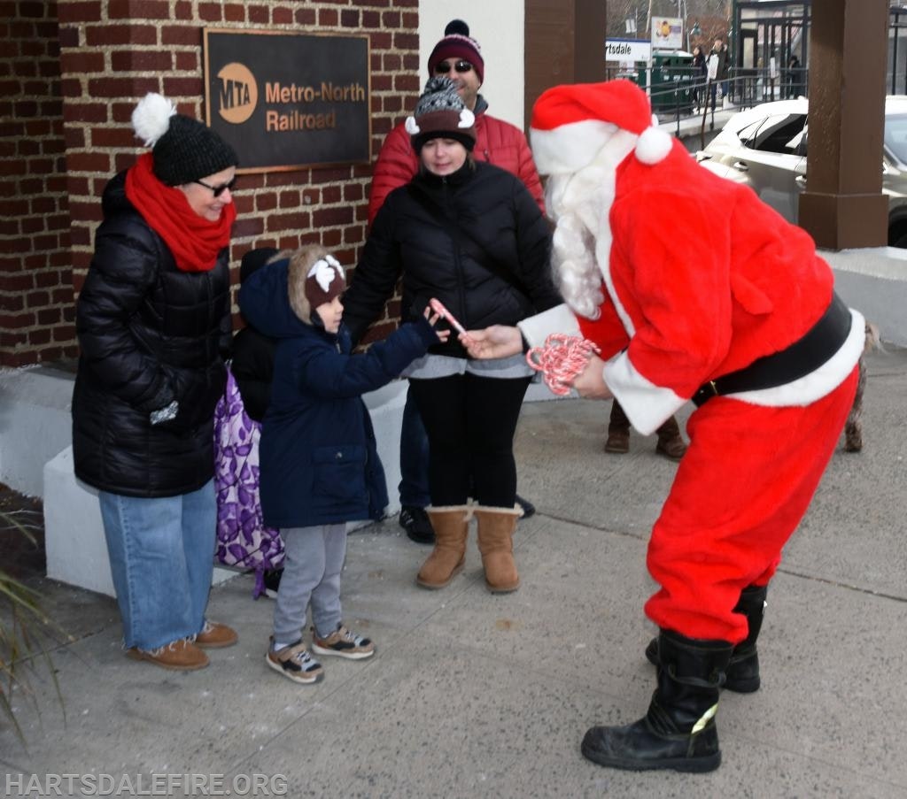 Santa giving candy canes to children at a Metro-North Railroad station.