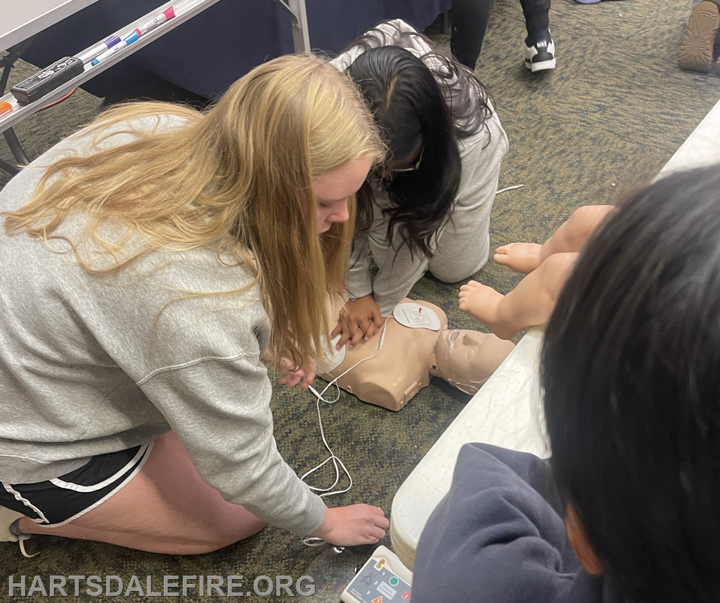 Two students practicing CPR techniques on a training mannequin, with another student observing.