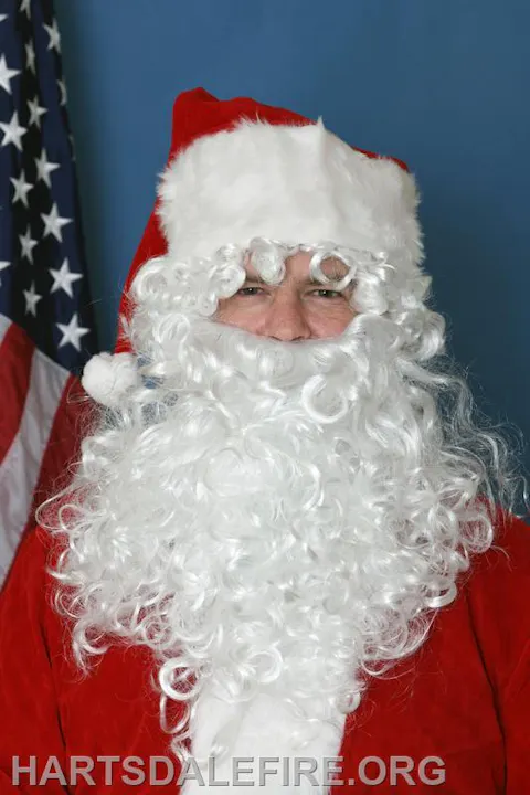 The image features a person dressed as Santa Claus, with a white beard and red suit, standing near an American flag.