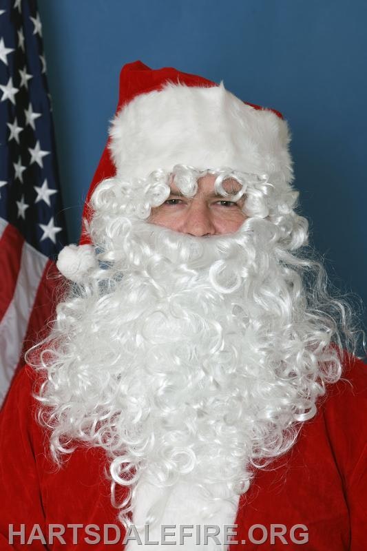 The image features a person dressed as Santa Claus, with a white beard and red suit, standing near an American flag.
