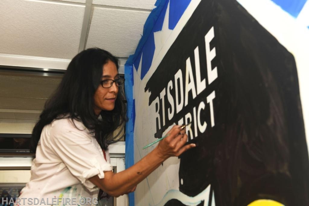 A person painting a mural with the text "HARTSDALE DISTRICT" in white on a black background.