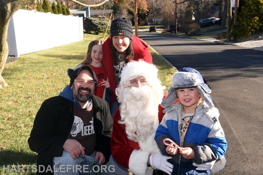 A cheerful group features Santa Claus with children and adults, enjoying a festive moment outside.