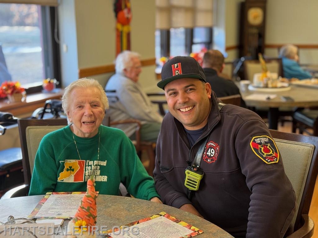 A woman and a man in firefighter gear smile together at a table, likely in a communal dining setting.