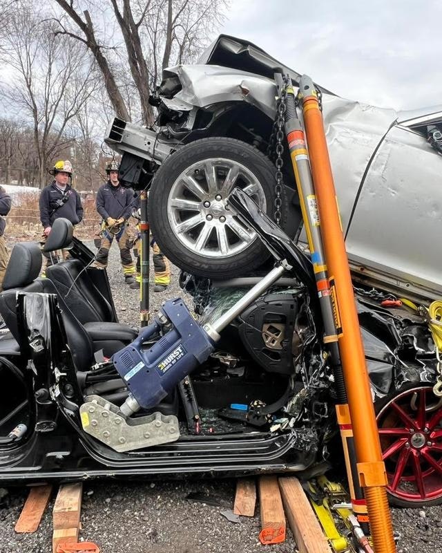 A severely damaged car is overturned, and rescue workers are on-site, likely responding to an accident.