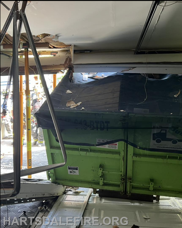 A damaged ceiling with a green dumpster visible, indicating impact. Firefighters are present, likely assessing the situation.