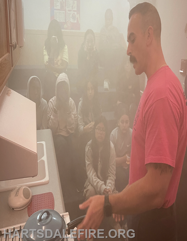 A firefighter demonstrates safety in a smoky environment to a group of attentive students.