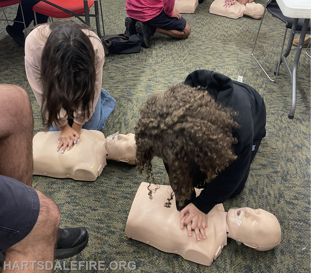 Two individuals are practicing CPR on training mannequins in a classroom setting.