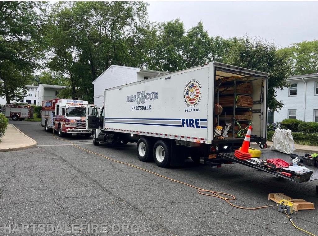 Fire trucks and a fire department utility truck parked on a street near residential buildings, with equipment on display.
