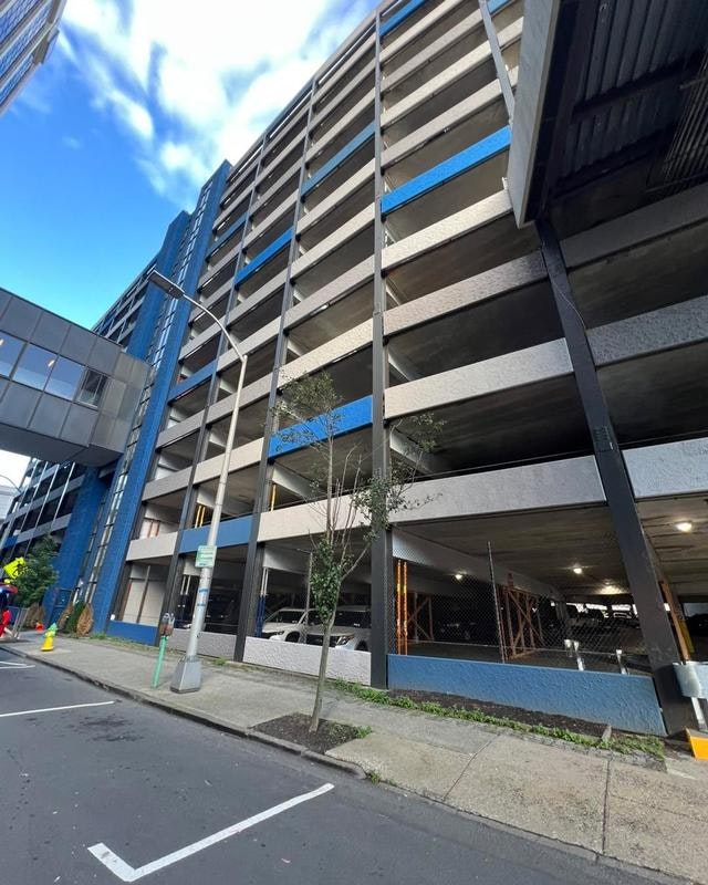 A multi-level parking garage with a blue and gray facade, connected by a walkway to a nearby building.