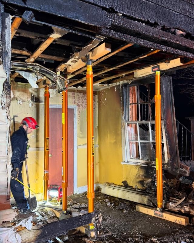 A firefighter inspects a damaged room with structural supports after a fire, showing signs of charring and destruction.