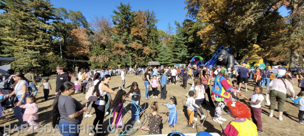 A lively outdoor event with many people, including families and children, participating in various activities and enjoying a festive atmosphere.